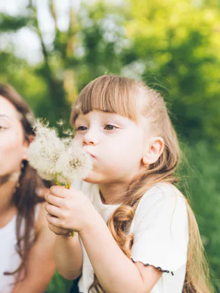 Mother and daughter having fun blowing dandelions