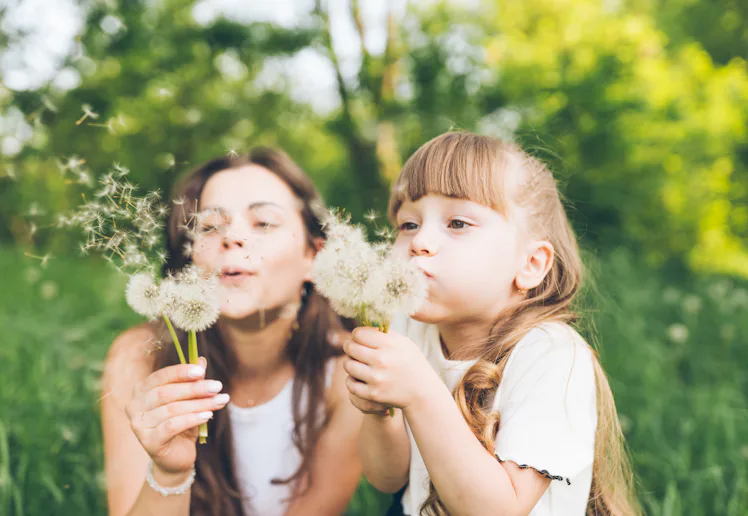 Mother and daughter having fun blowing dandelions
