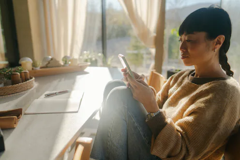 Photo of a mid adult Asian woman sitting in a comfort of her home and performing daily check up of a...