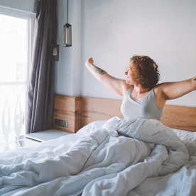 Middle age curly woman wake up in the morning full of happiness and strength and look to the window....