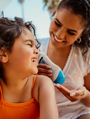 Mother putting sunscreen on her daughter before going into the pool