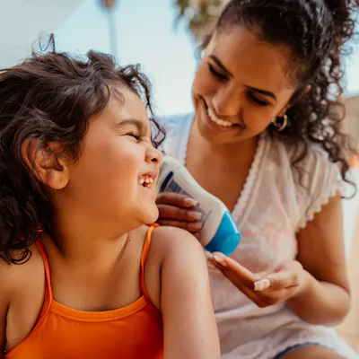 Mother putting sunscreen on her daughter before going into the pool