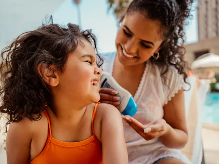 Mother putting sunscreen on her daughter before going into the pool