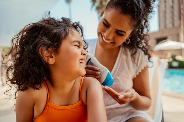 Mother putting sunscreen on her daughter before going into the pool