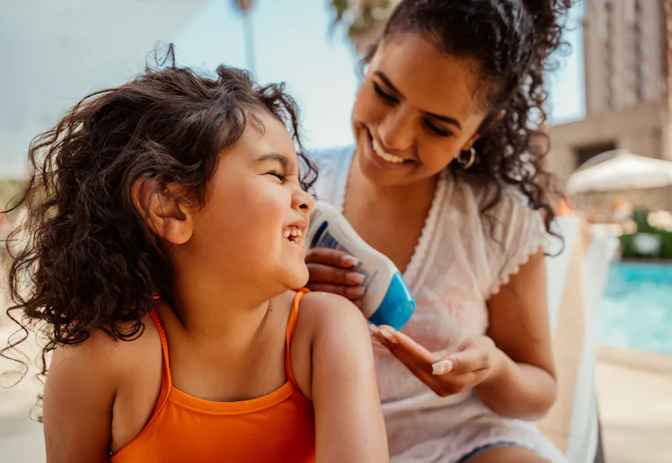 Mother putting sunscreen on her daughter before going into the pool
