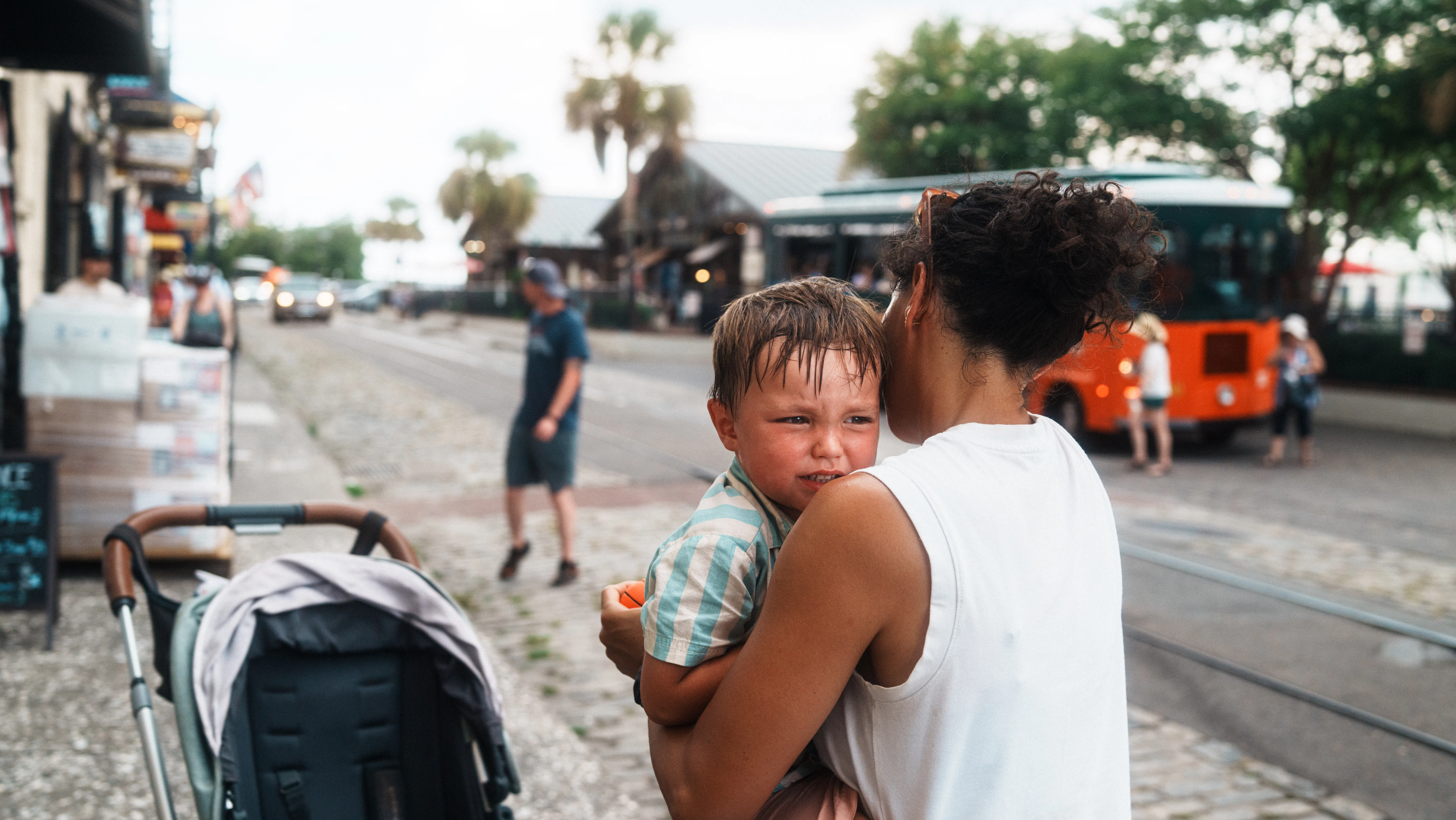 A concerned mother cradles her crying child while walking along a vibrant street in Savannah, Georgi...