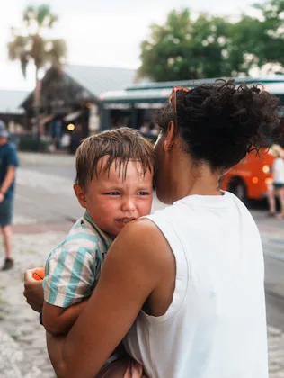 A concerned mother cradles her crying child while walking along a vibrant street in Savannah, Georgi...