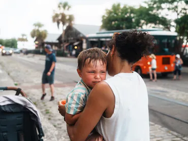 A concerned mother cradles her crying child while walking along a vibrant street in Savannah, Georgi...