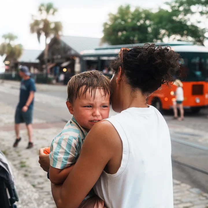 A concerned mother cradles her crying child while walking along a vibrant street in Savannah, Georgi...