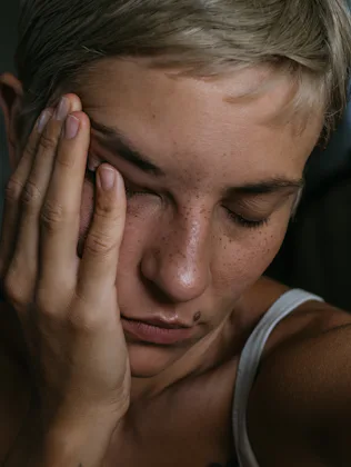 A horizontal closeup portrait of a young woman in natural lighting on a dark background holding hand...