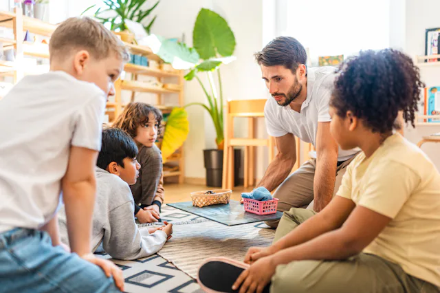 Diverse children and teacher sitting on a floor mat, working together with educational materials and...
