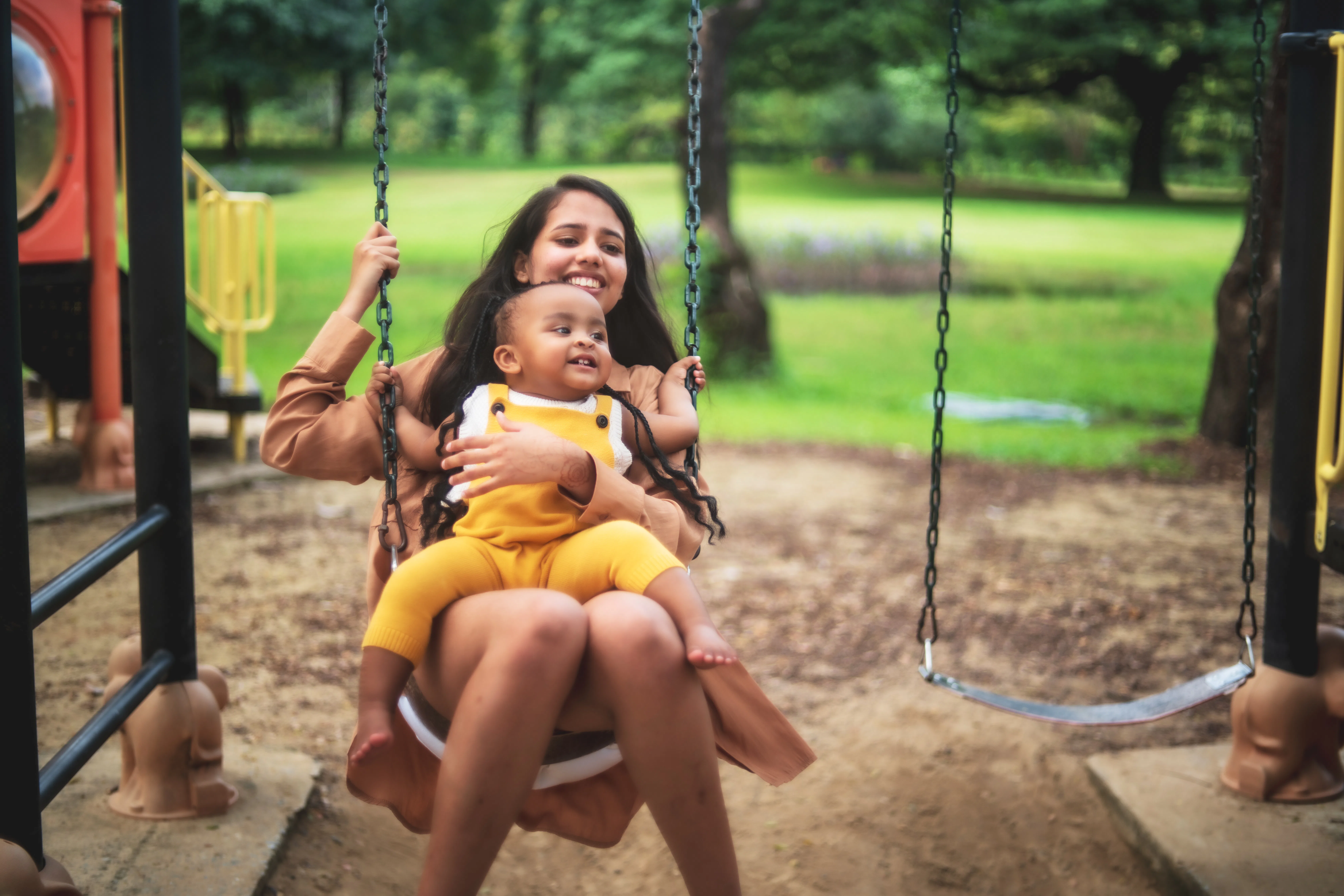 A young woman with a baby on her lap swings. 
