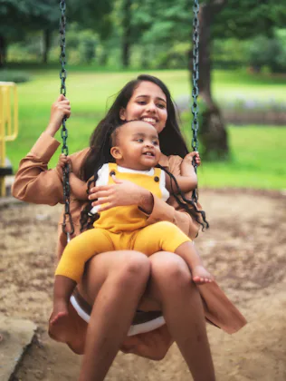 A young woman with a baby on her lap swings.