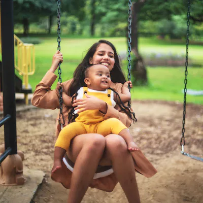 A young woman with a baby on her lap swings.