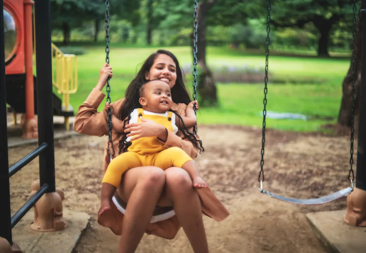 A young woman with a baby on her lap swings.