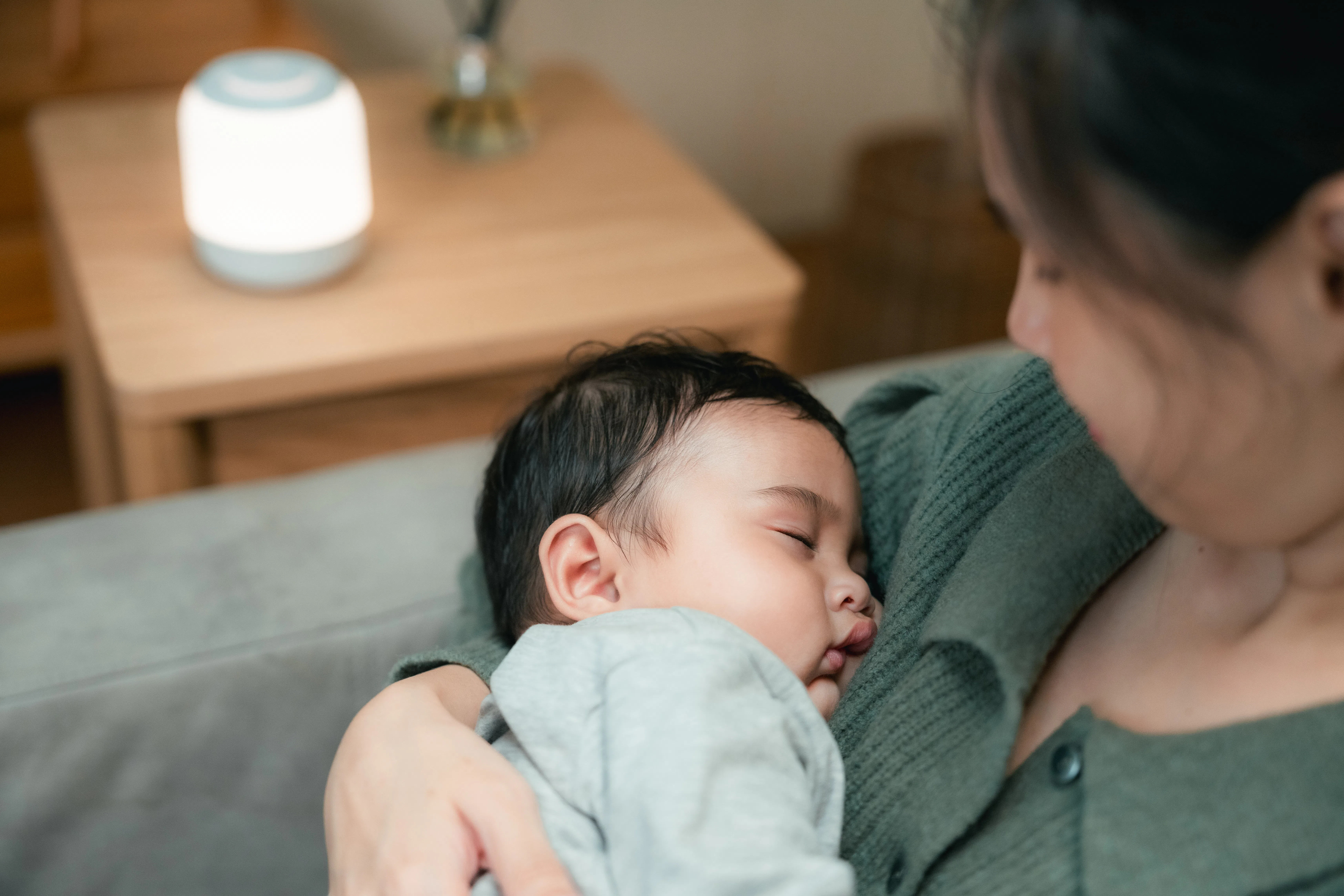 Young mother gently carrying her sleeping baby, offering comfort through closeness and calm, reflect...