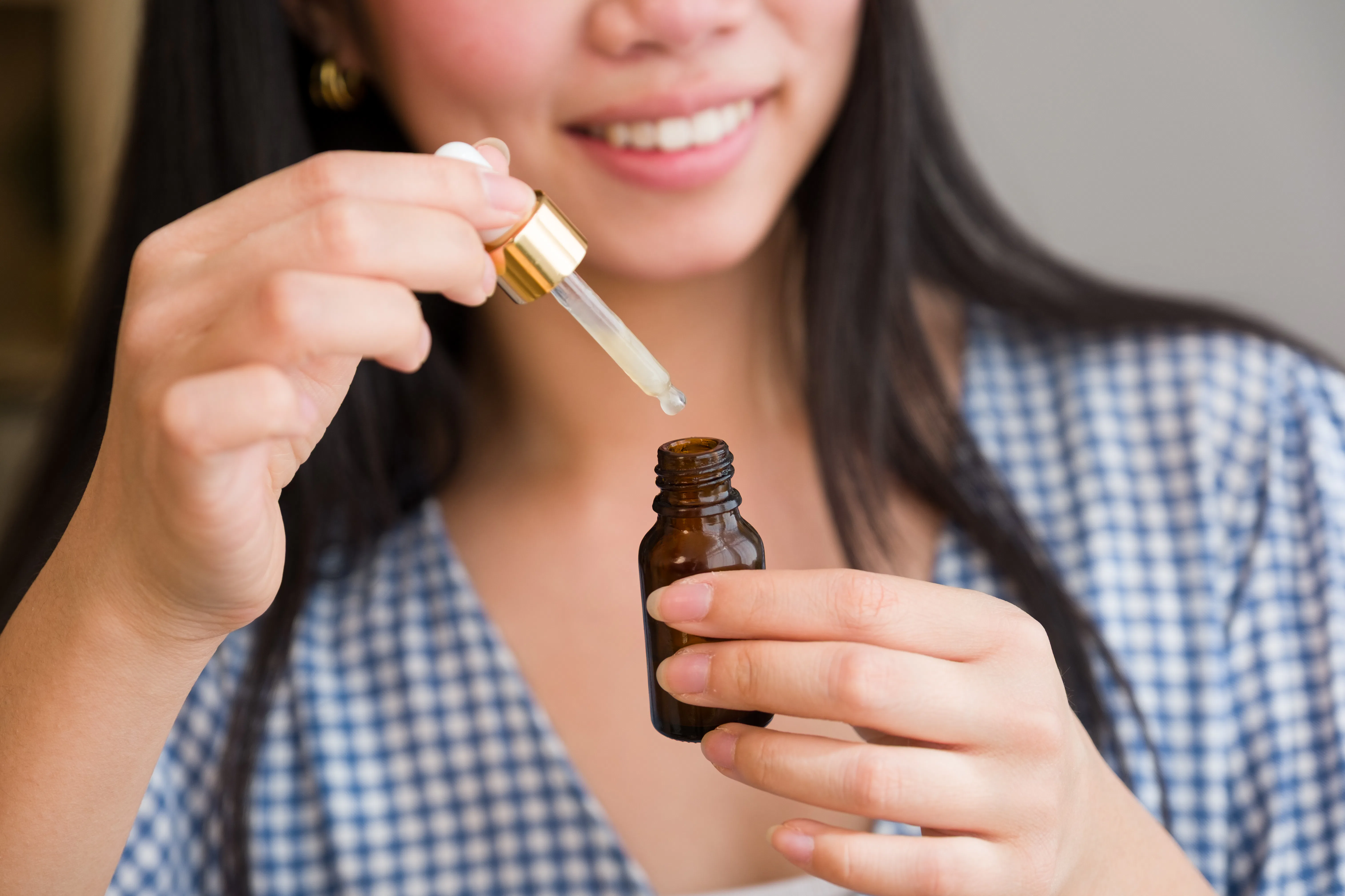 Young adult woman smiling, holding a dropper bottle with natural facial serum