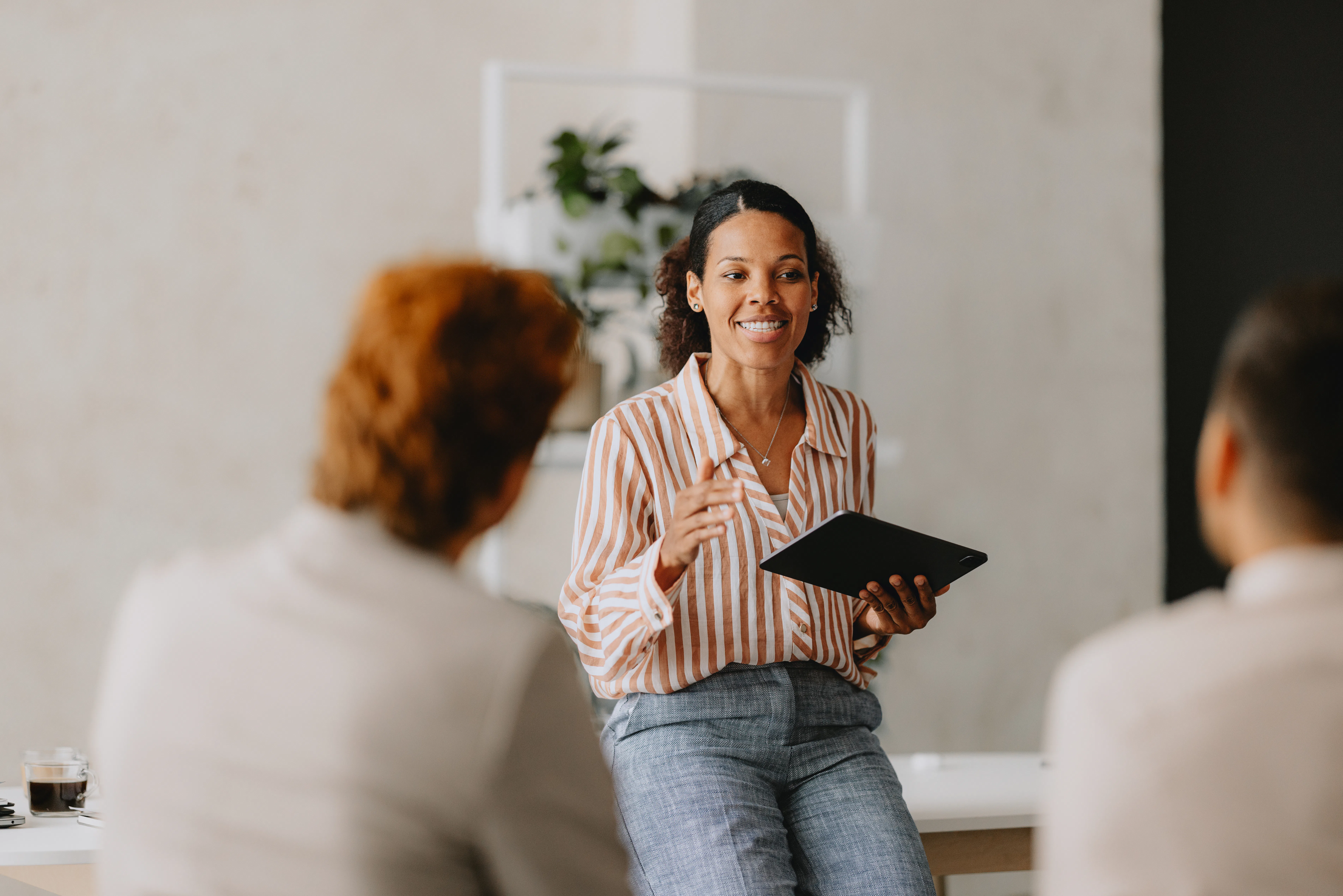 Confident businesswoman leading a group business meeting at a bright beige office. Professional inte...