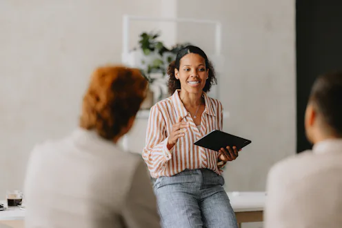 Confident businesswoman leading a group business meeting at a bright beige office. Professional inte...