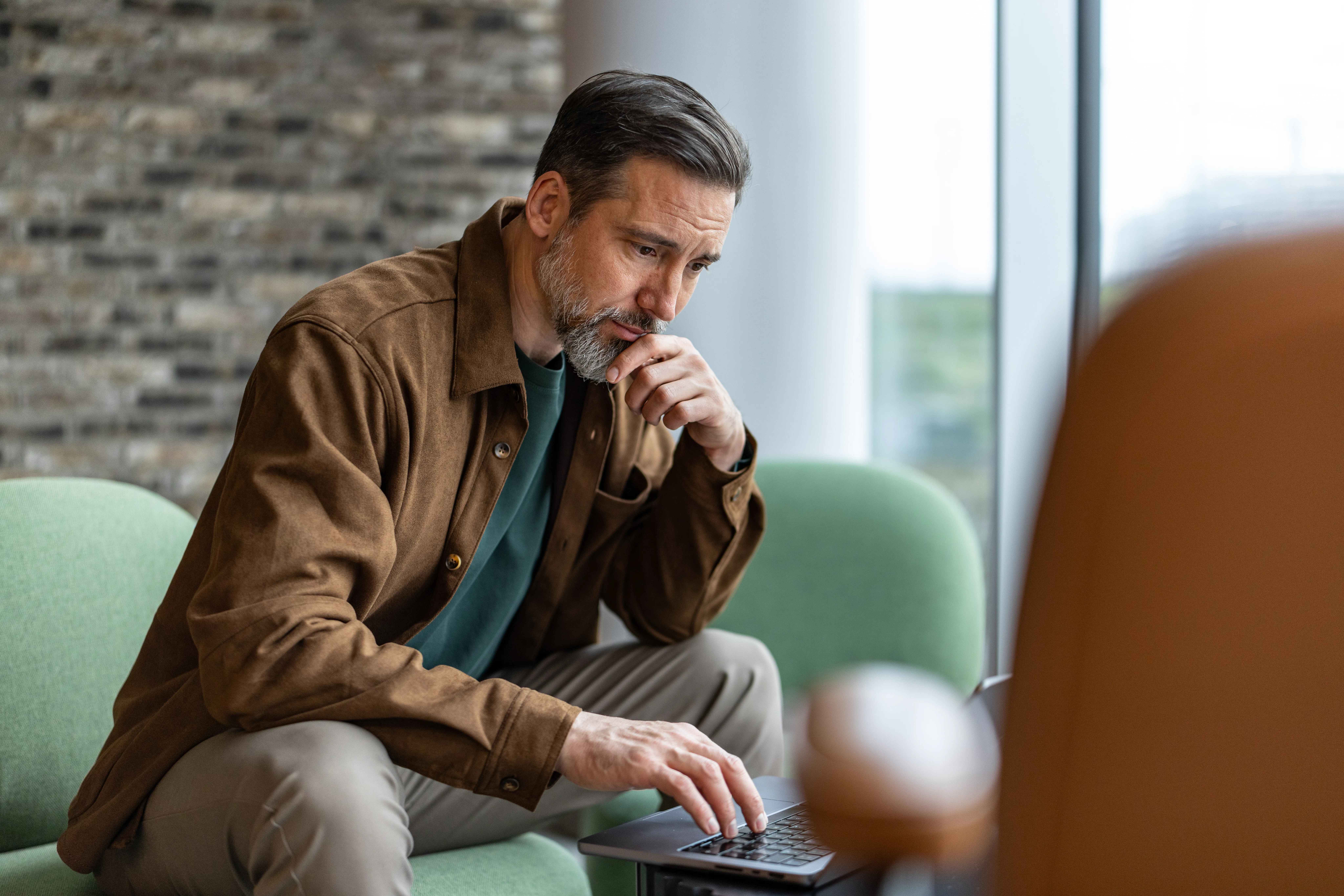 Businessman concentrating on his work, sitting in a modern office or coworking space, using a laptop...
