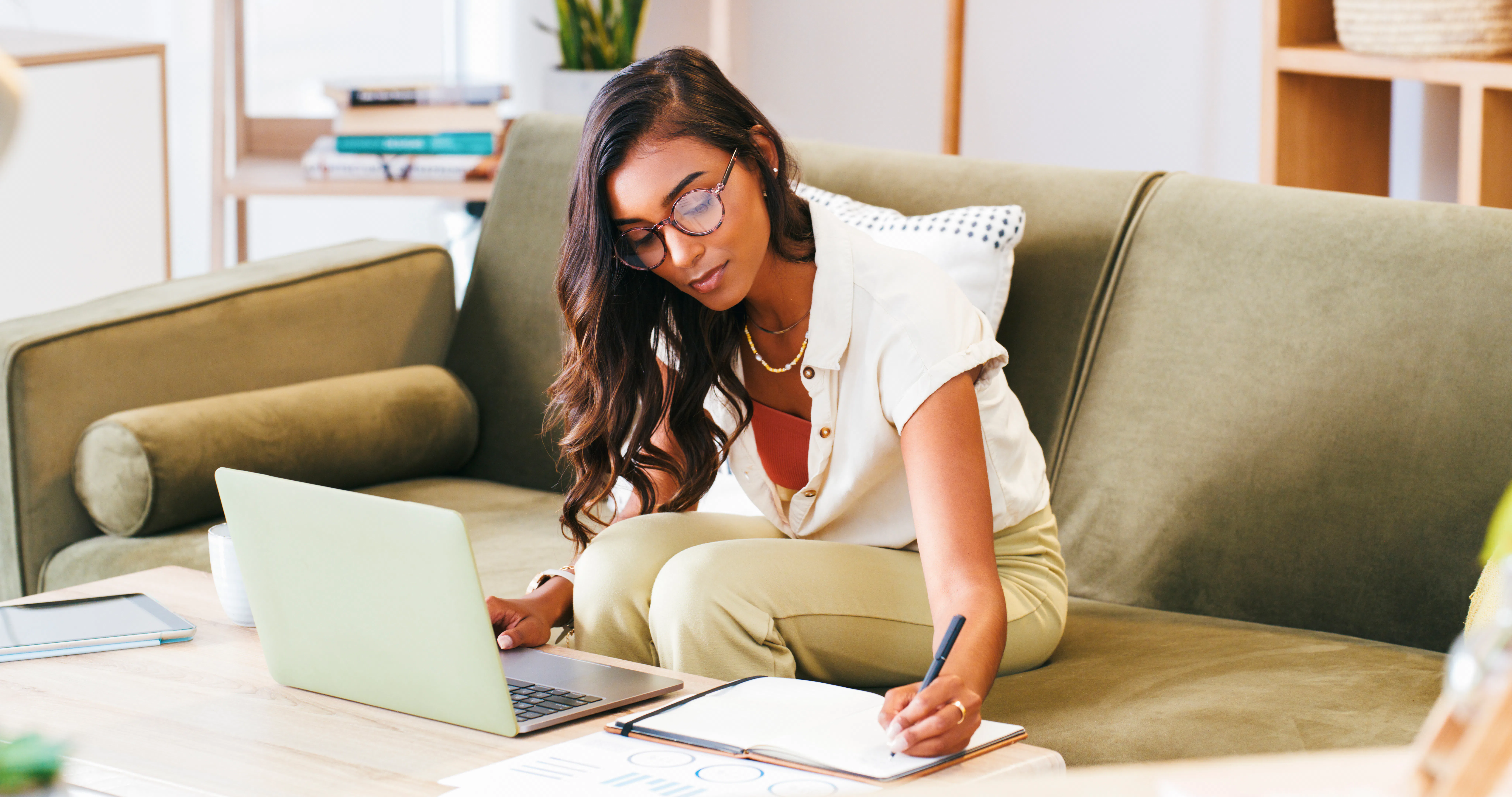Woman, writing and planning on sofa with notebook, laptop and research for online education or e lea...