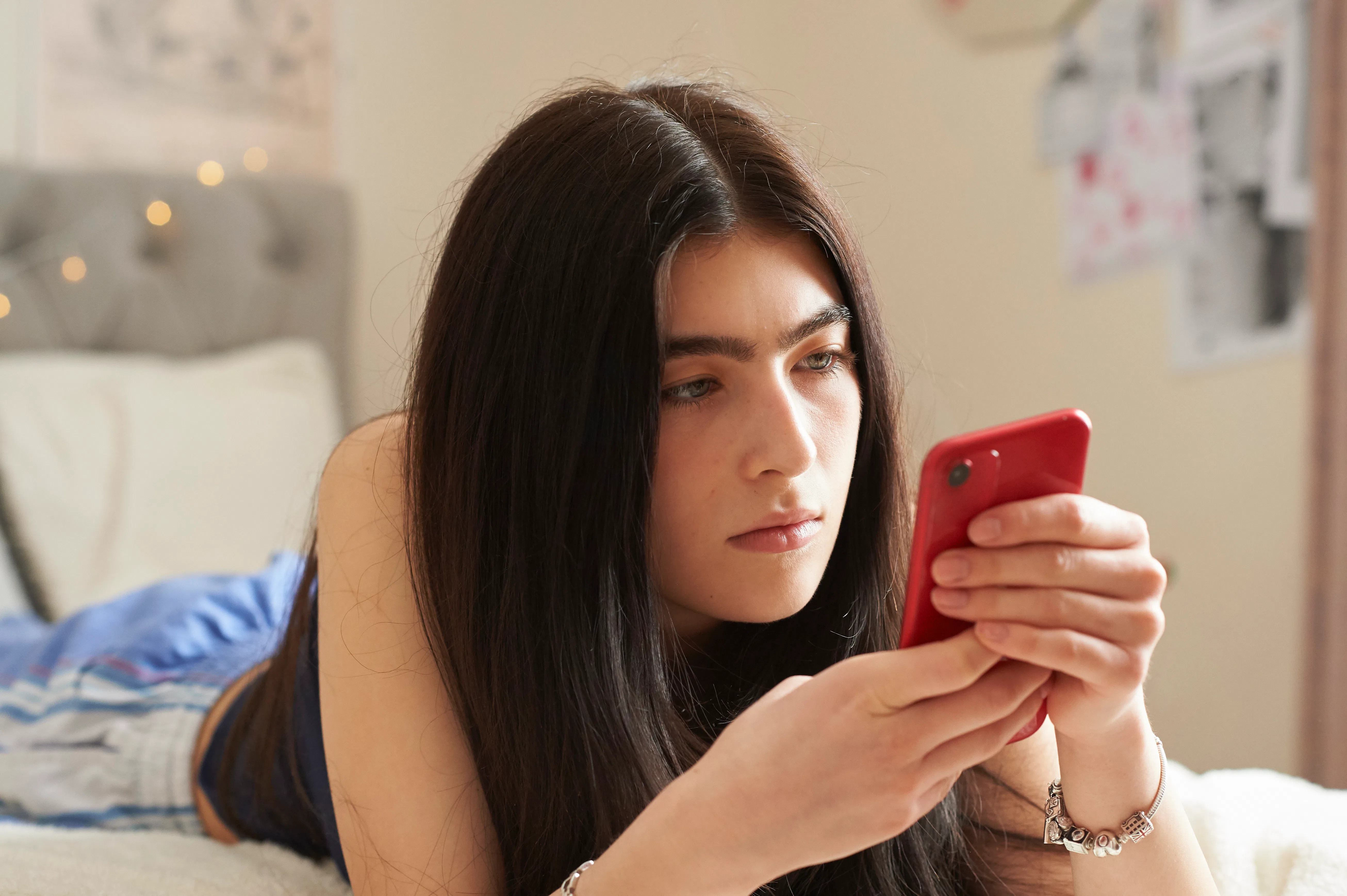 Teenage girl lying on her bed using a smart phone
