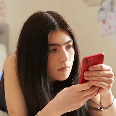 Teenage girl lying on her bed using a smart phone