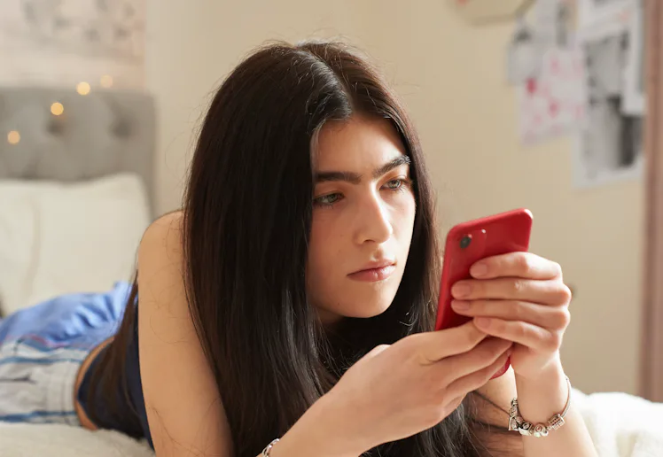Teenage girl lying on her bed using a smart phone