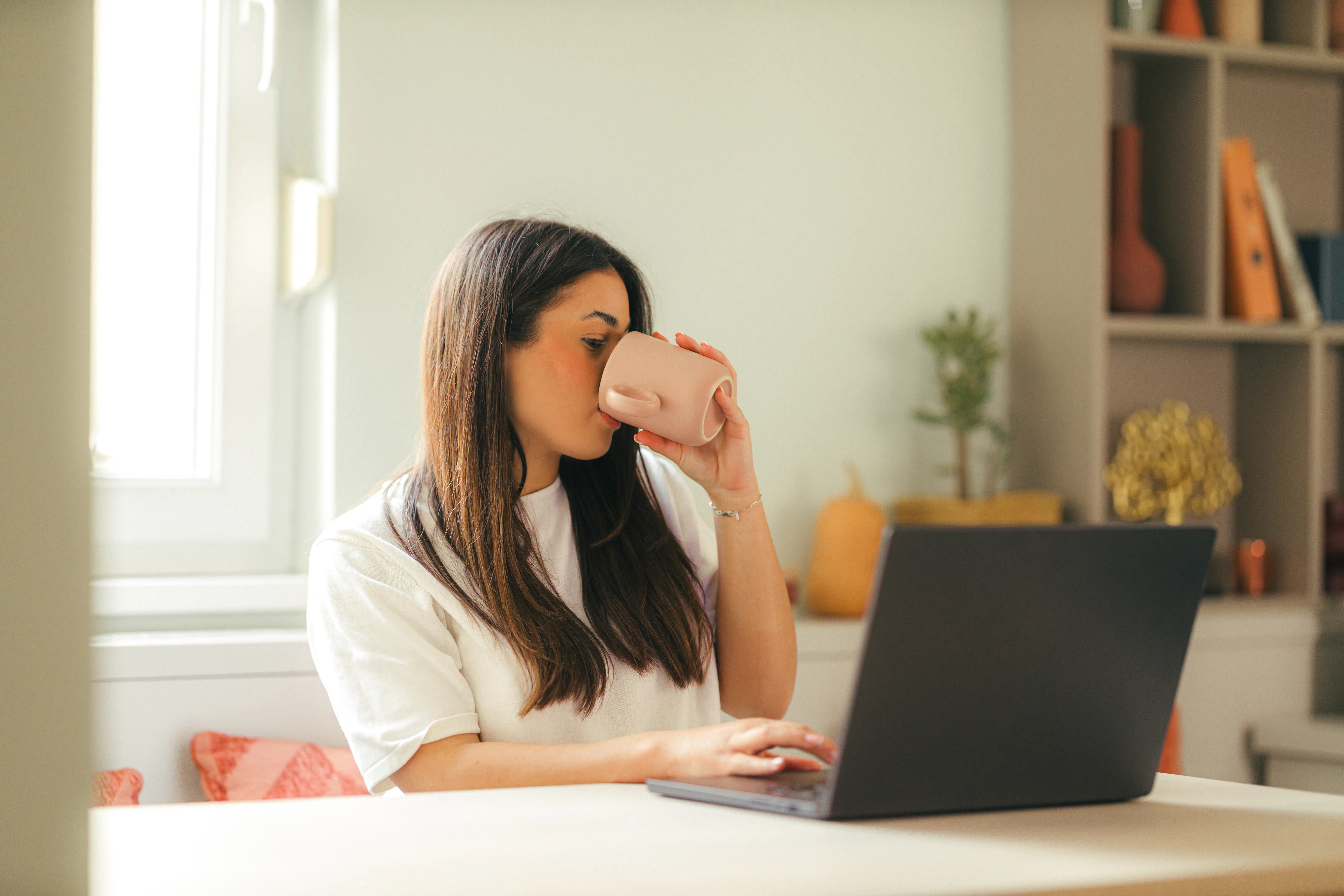 Young adult woman working on laptop indoors in modern apartment during daytime, wearing casual cloth...