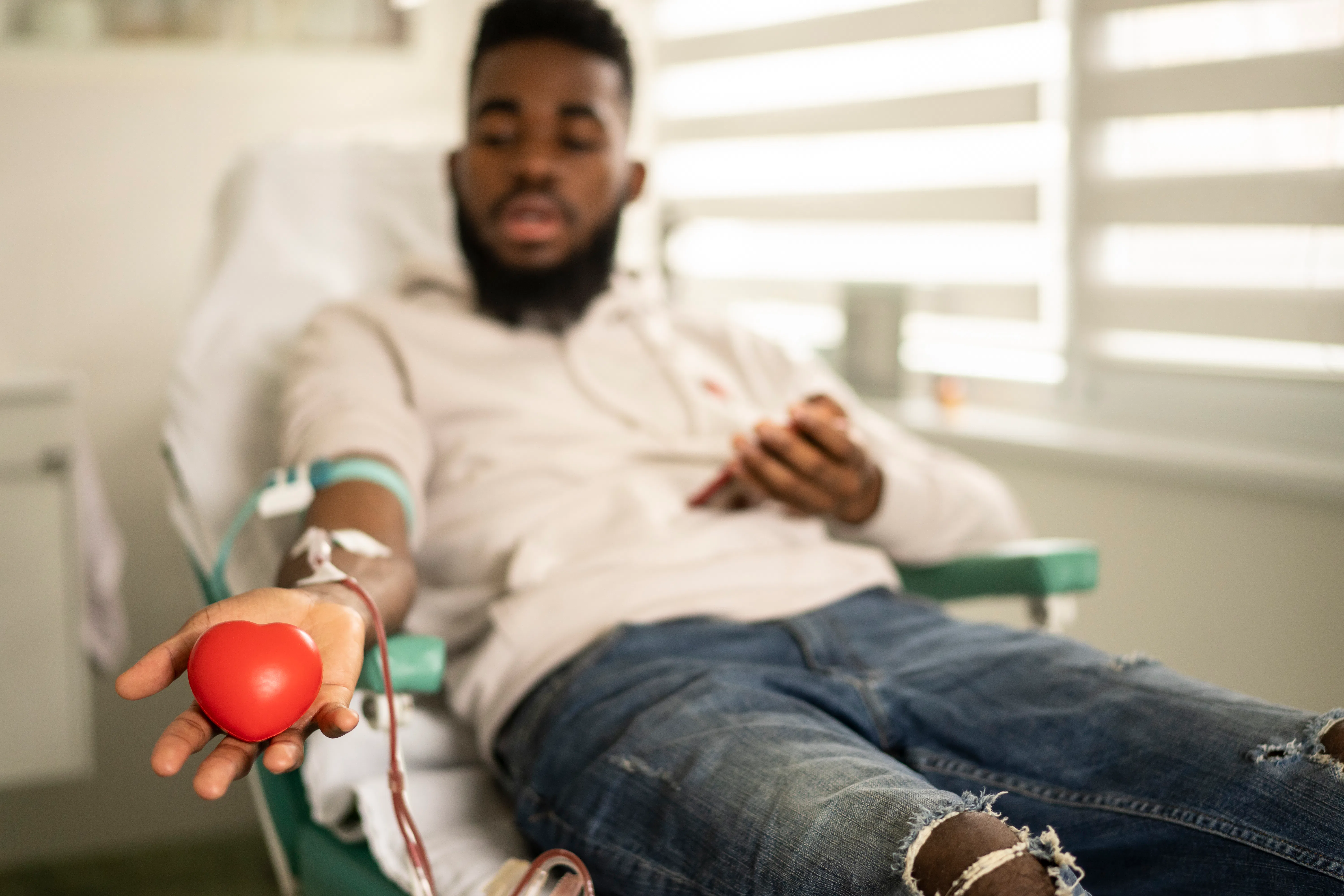 A male donor, lying down, shows the heart-shaped ball for  blood donation at the modern blood donati...