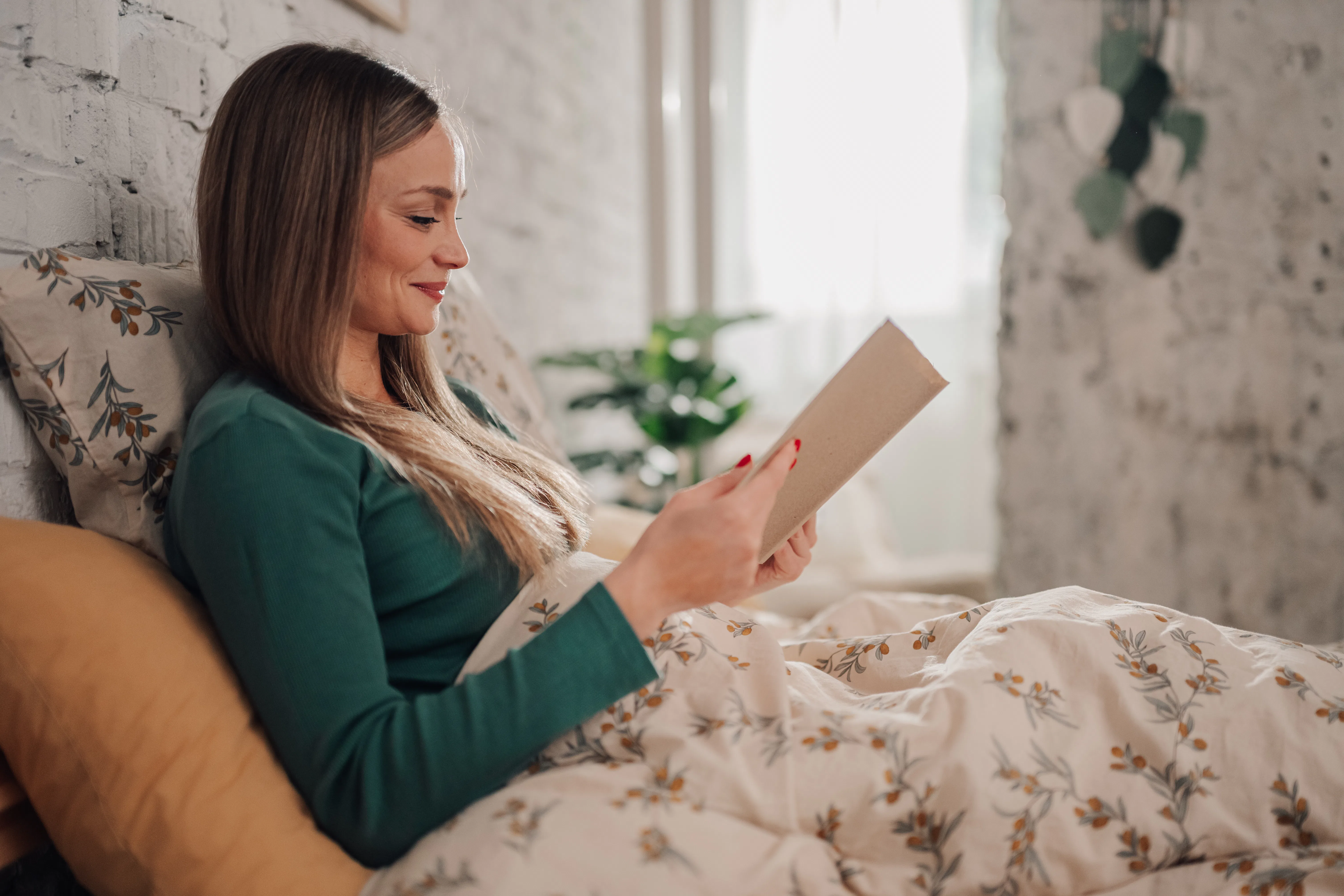 Young woman in her twenties lounging in bed in the morning, engrossed in a book. Embracing a serene ...