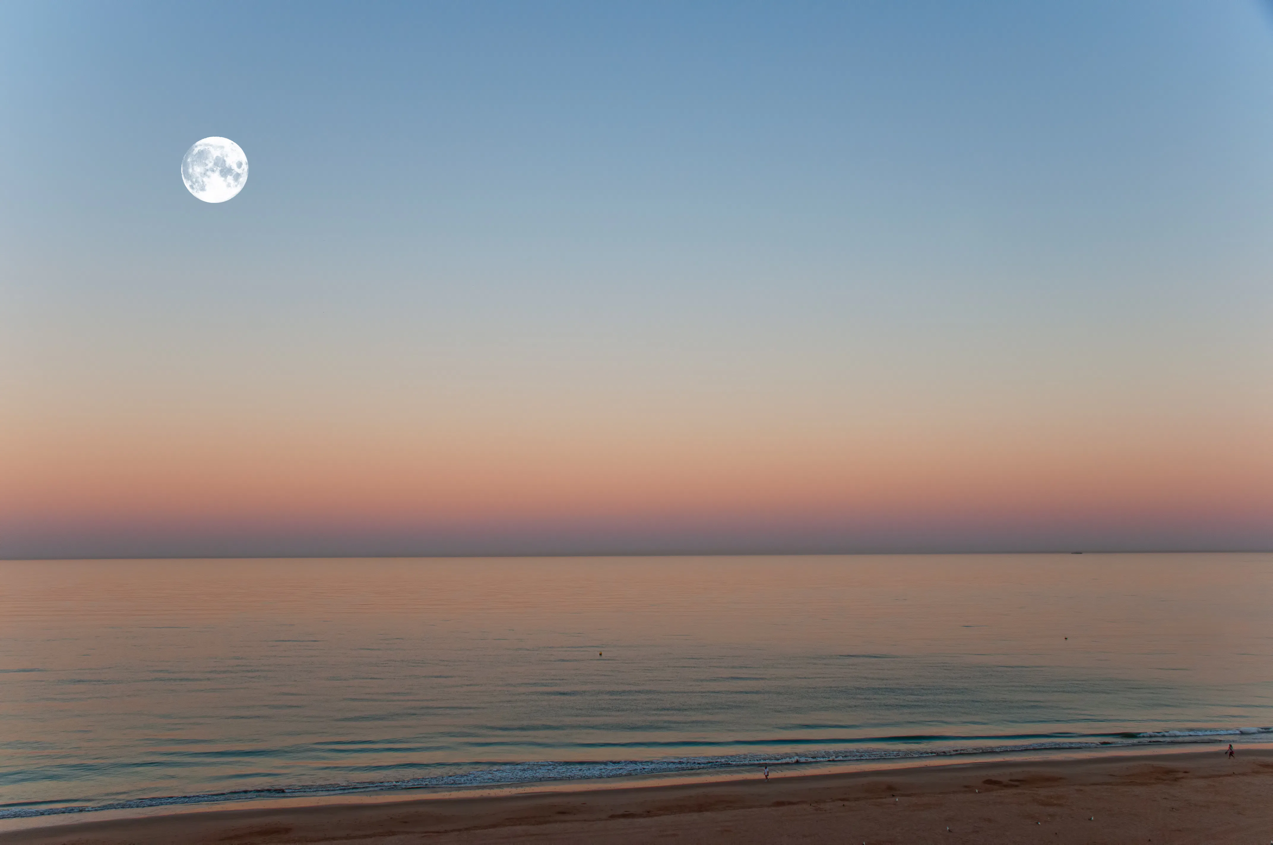 Pastel colored dawn skies & a full moon over the Atlantic Ocean in summertime, Cadiz, Andalucia, Spa...