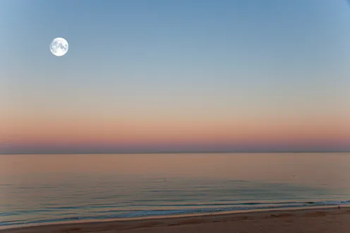 Pastel colored dawn skies & a full moon over the Atlantic Ocean in summertime, Cadiz, Andalucia, Spa...