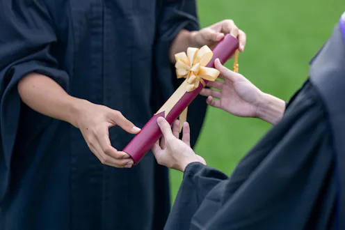 Close-up of a student receiving a diploma during an outdoor graduation ceremony.