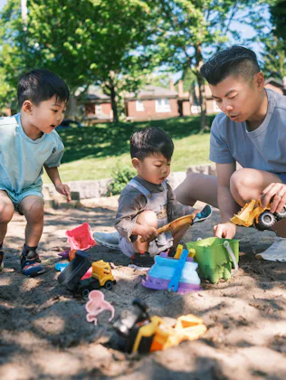 Young father and two sons playing in the sandbox at the park. All dressed in casual summer clothing...