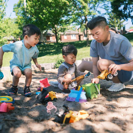 Young father and two sons playing in the sandbox at the park. All dressed in casual summer clothing...