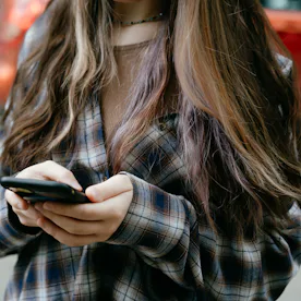 A close-up view of a young woman interacting with her smartphone while outdoors. She wears a casual ...