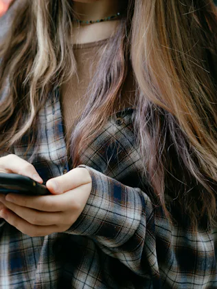 A close-up view of a young woman interacting with her smartphone while outdoors. She wears a casual ...
