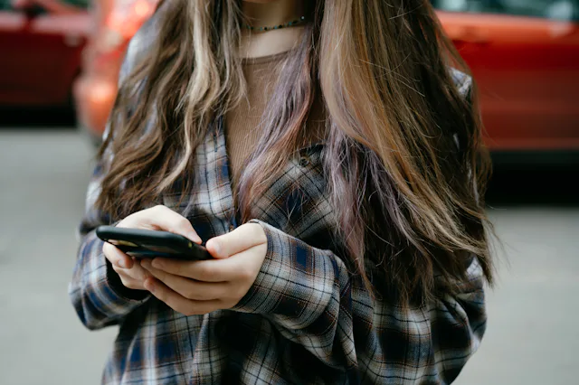 A close-up view of a young woman interacting with her smartphone while outdoors. She wears a casual ...