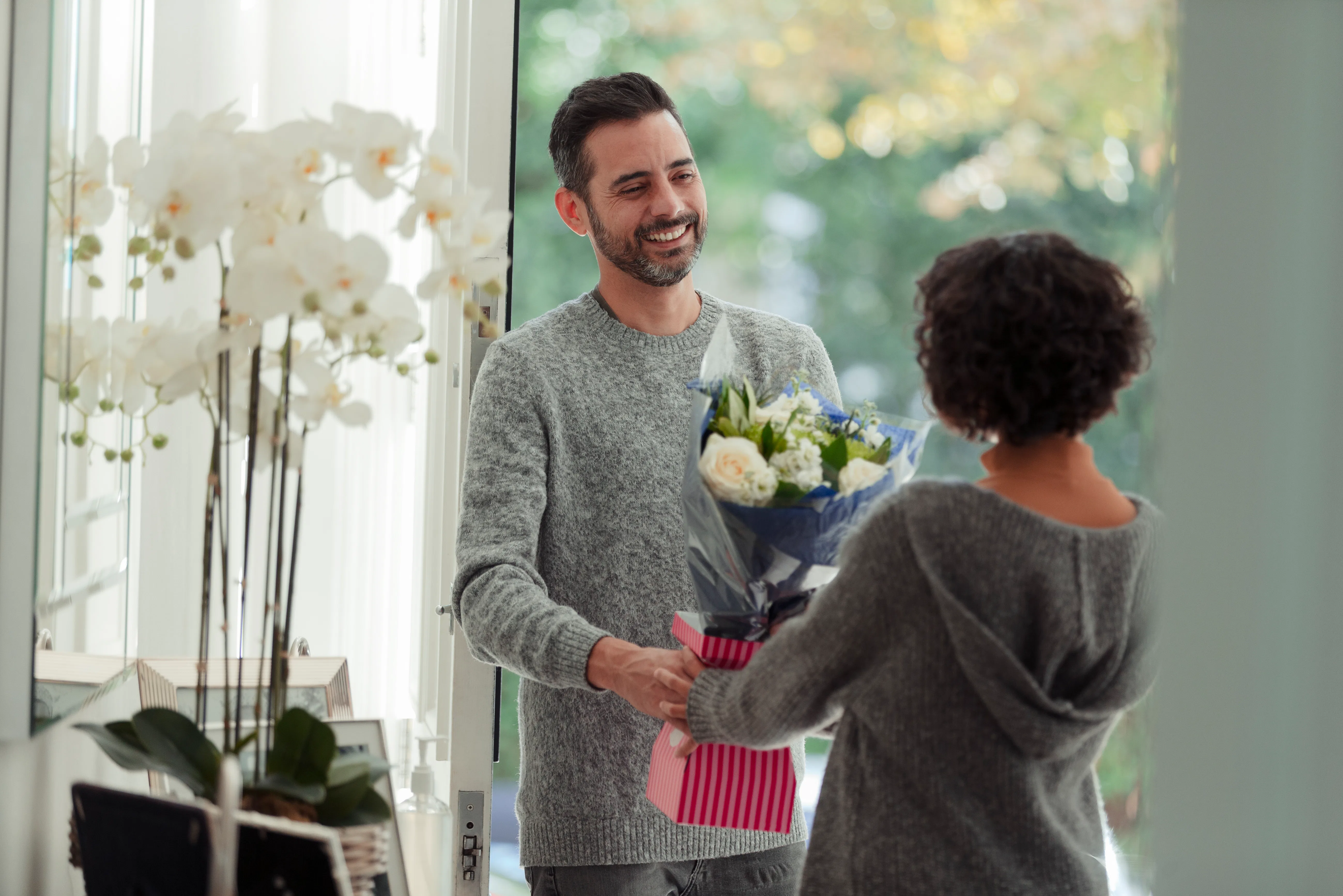 Happy husband surprising wife with flower bouquet at front door of home