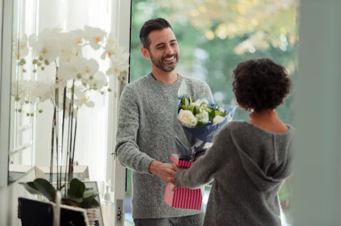 Happy husband surprising wife with flower bouquet at front door of home