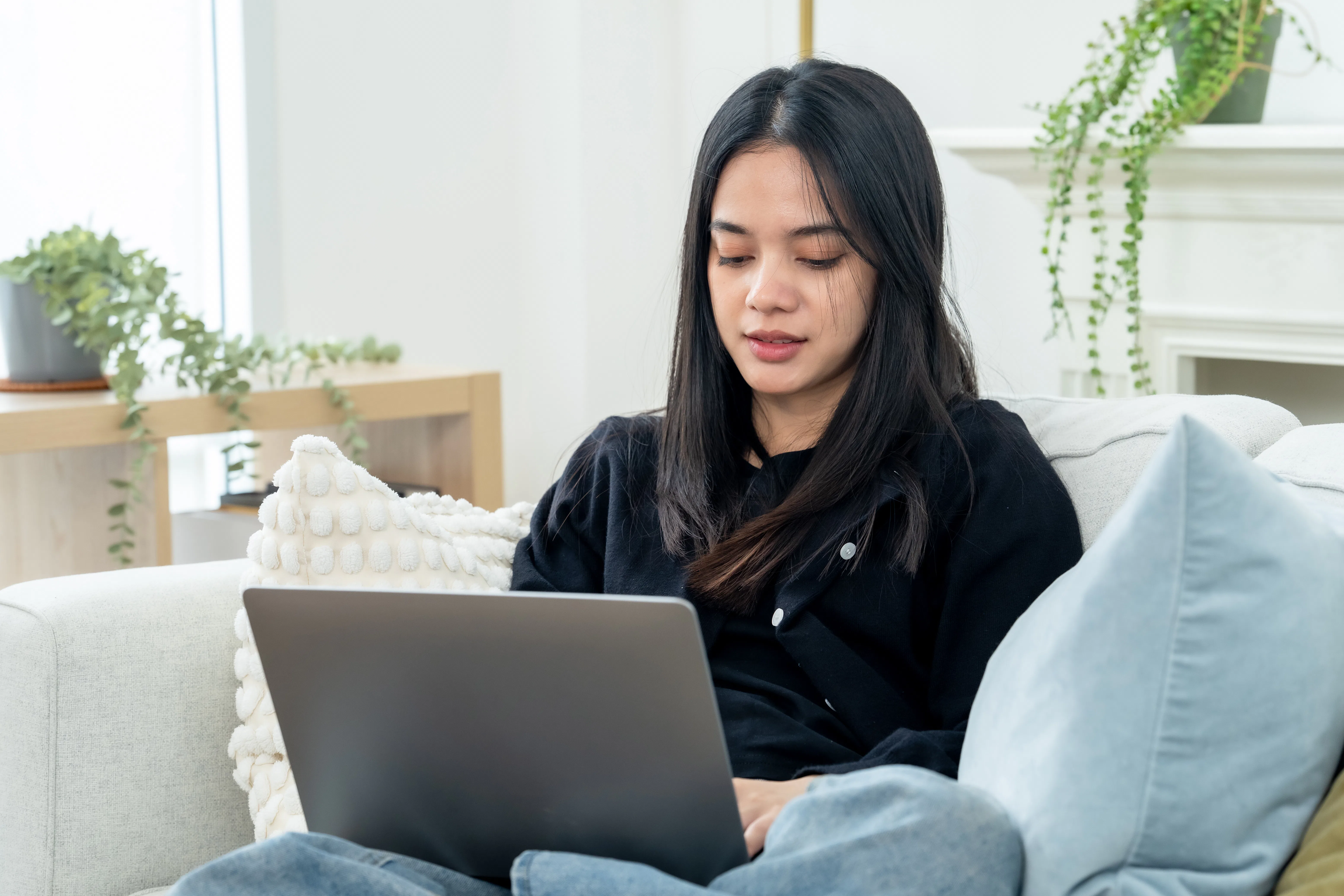Asian working woman looks at laptop with tired serious mood on sofa at home, spending weekend stayca...