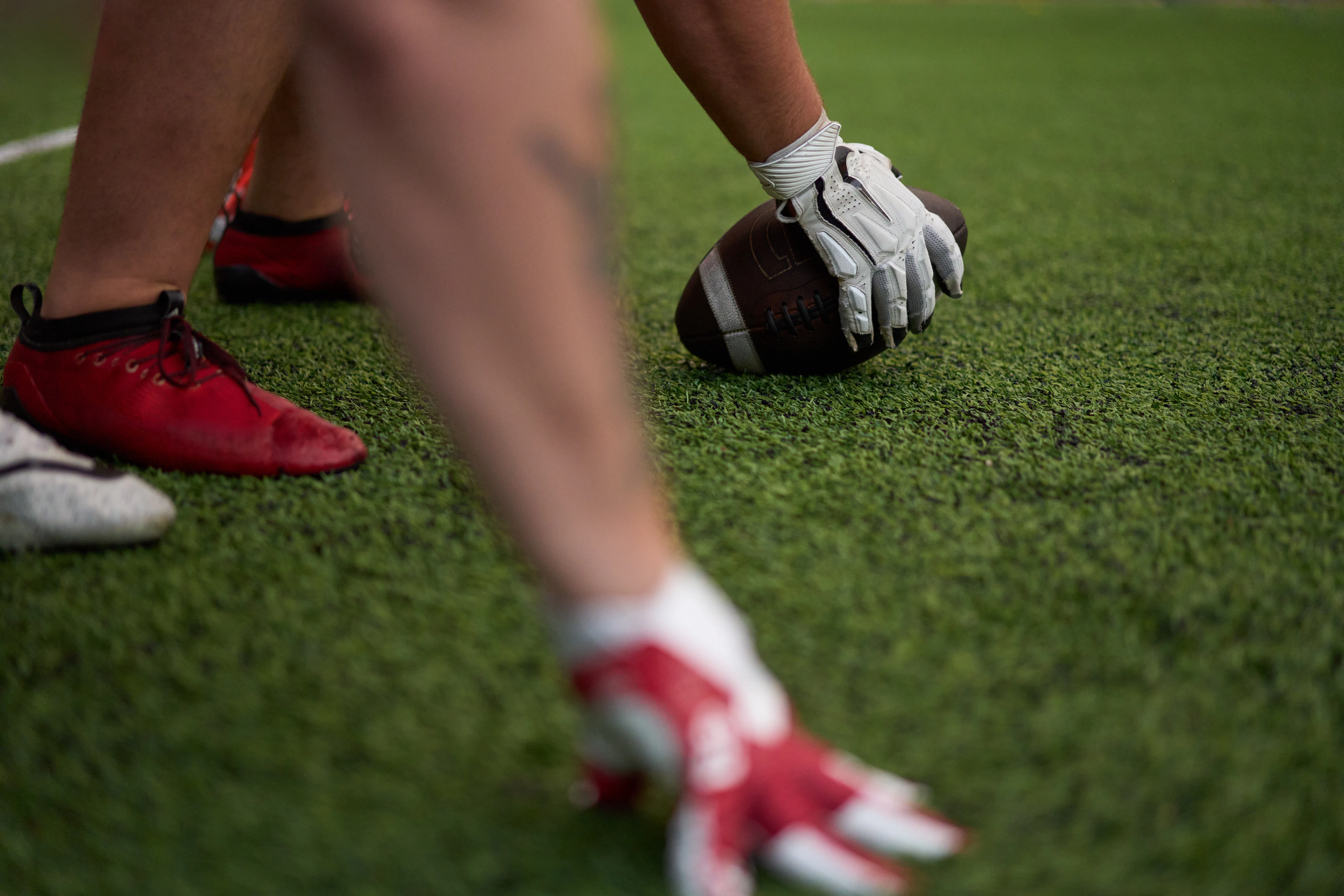 Close-up of football players in position on the field, with one player holding the ball, ready for t...