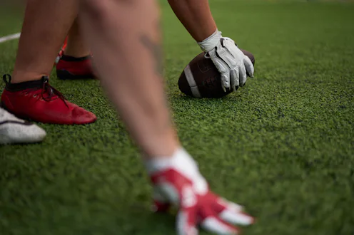 Close-up of football players in position on the field, with one player holding the ball, ready for t...
