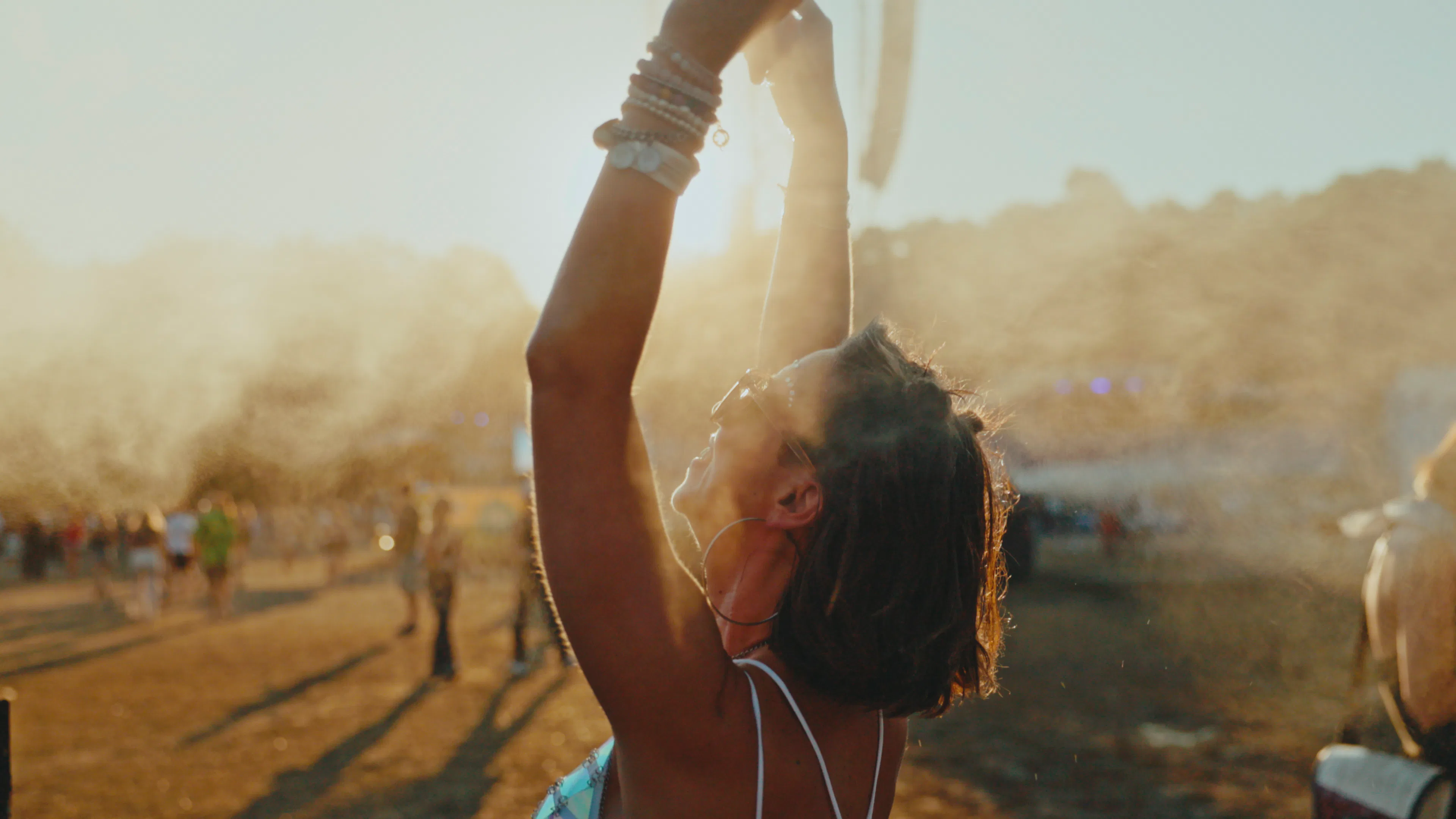 A cheerful young Caucasian female is standing with her arms raised, cooling off with mist at an outd...