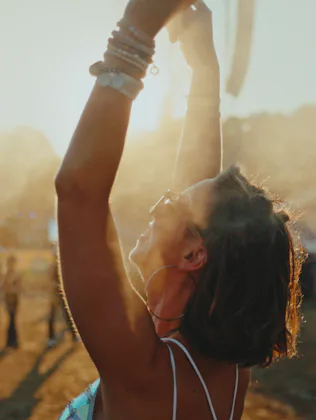 A cheerful young Caucasian female is standing with her arms raised, cooling off with mist at an outd...