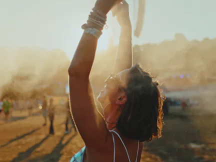 A cheerful young Caucasian female is standing with her arms raised, cooling off with mist at an outd...