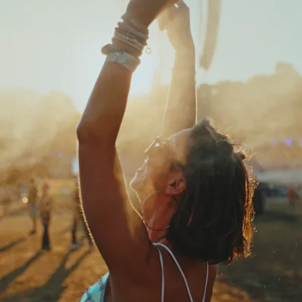 A cheerful young Caucasian female is standing with her arms raised, cooling off with mist at an outd...