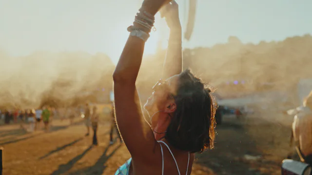 A cheerful young Caucasian female is standing with her arms raised, cooling off with mist at an outd...