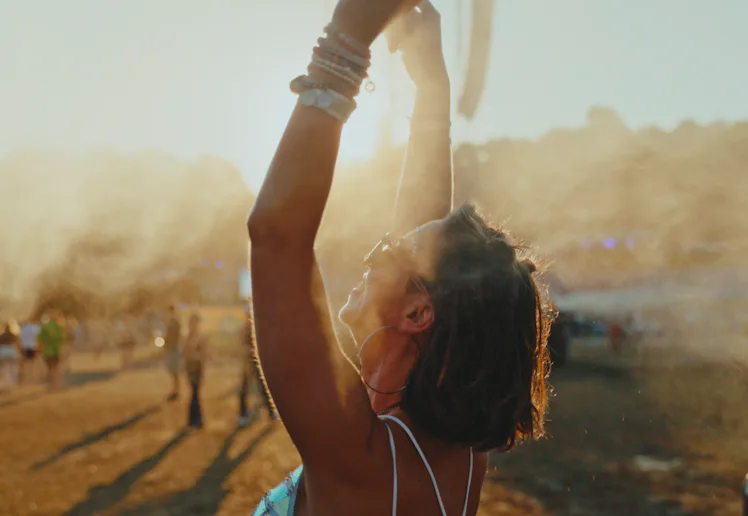 A cheerful young Caucasian female is standing with her arms raised, cooling off with mist at an outd...